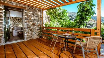 A wooden deck with a stone wall, a table with chairs, and a view of greenery and hills.