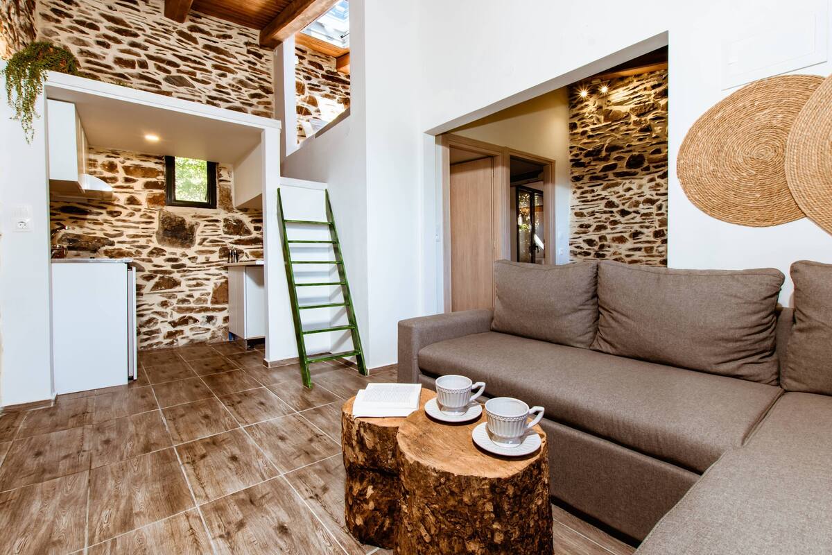 Un intérieur moderne avec un mur en pierre, un escalier en bois, un canapé et une petite table avec des tasses.