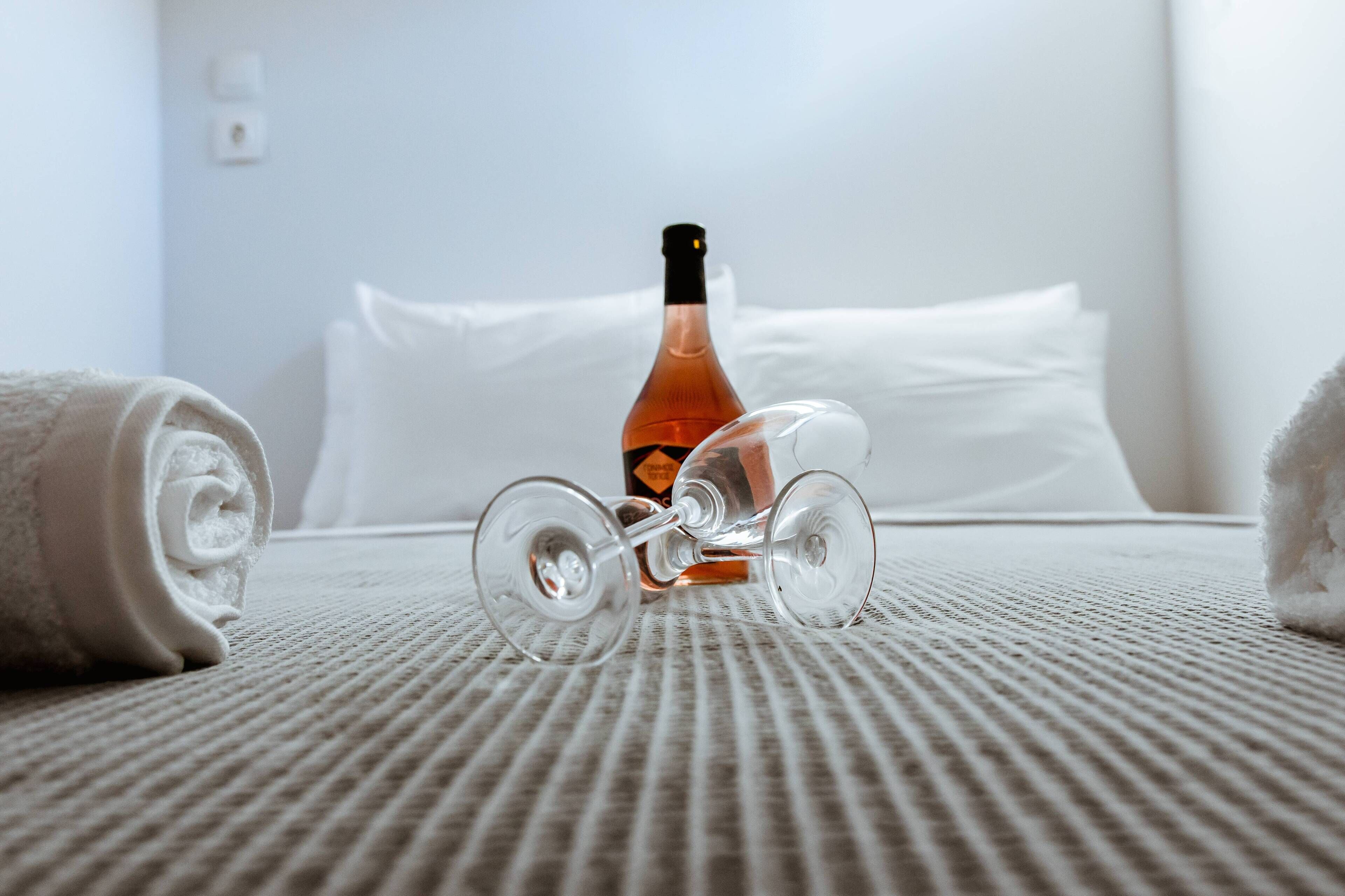A bed with a rolled towel, a bottle, and a wine glass on a textured bedspread.