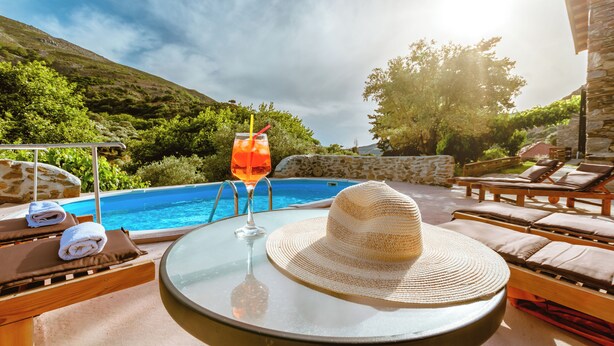 A poolside setting with lounge chairs, a glass table with a hat, and a drink. - Traditional Apartments Elafos (Kissamos)