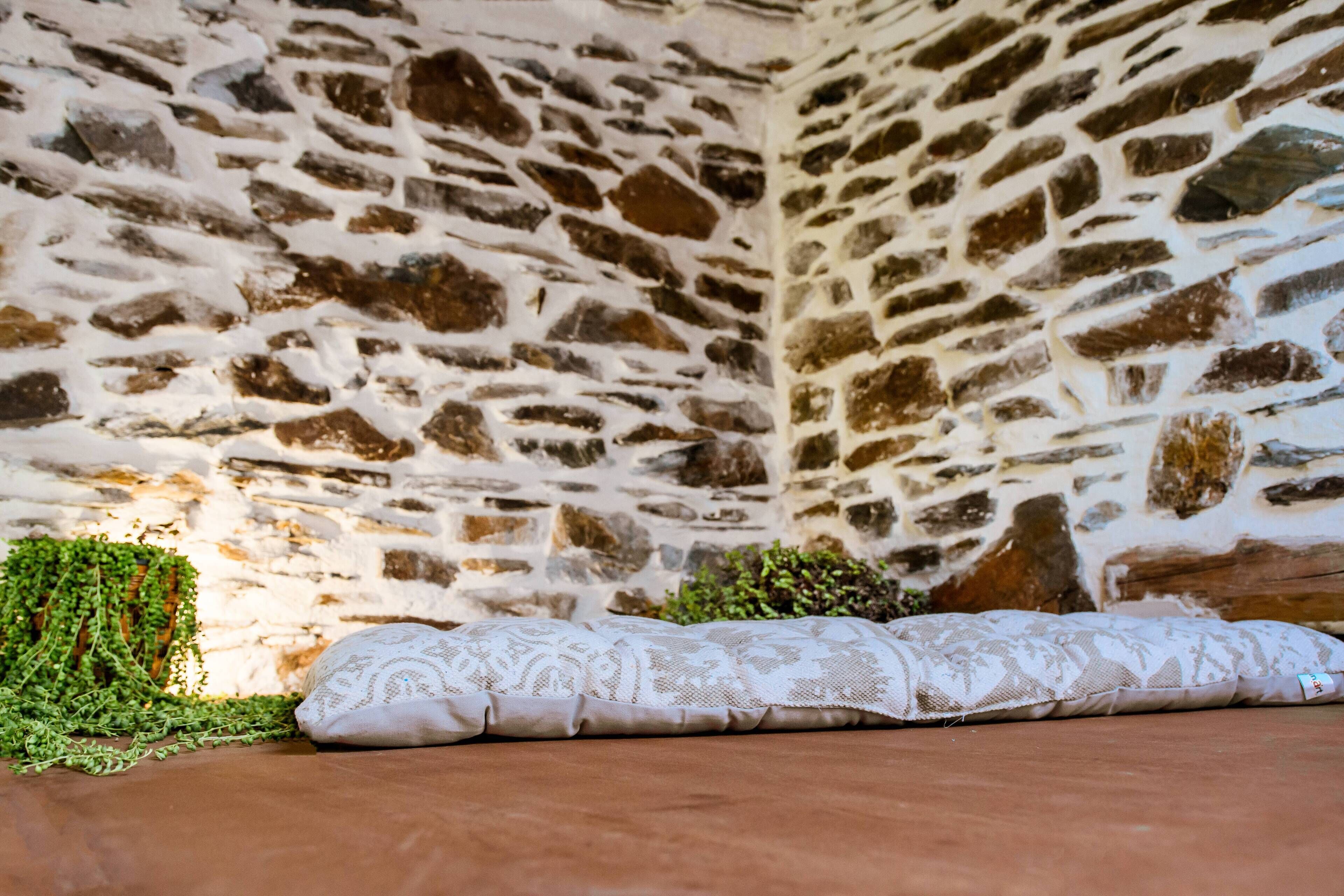 Interior de una pared de piedra con un cojín estampado en el suelo.