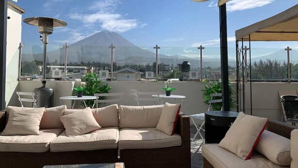 A rooftop terrace with a sofa, chairs, and tables, overlooking a cityscape and a mountain. - IDEAL for WORK and confort JACUZZI and GRILL (Arequipa)