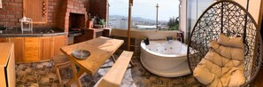 A kitchen with a brick oven, a dining table with benches, a hot tub, and a hanging chair.