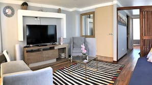 A living room with a TV, sofa, armchair, and a coffee table with a striped rug. - IDEAL for WORK and confort JACUZZI and GRILL (Arequipa)
