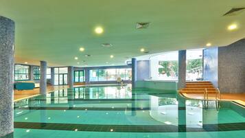 A large indoor swimming pool with clear glass walls, a tiled floor, and a staircase leading to an upper level.