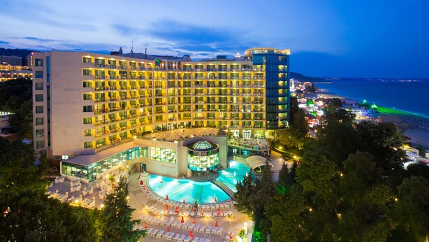 A hotel with multiple floors, a pool area, and a view of the sea.