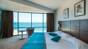 A hotel room with a large window, a bed, a chair, and a small table.