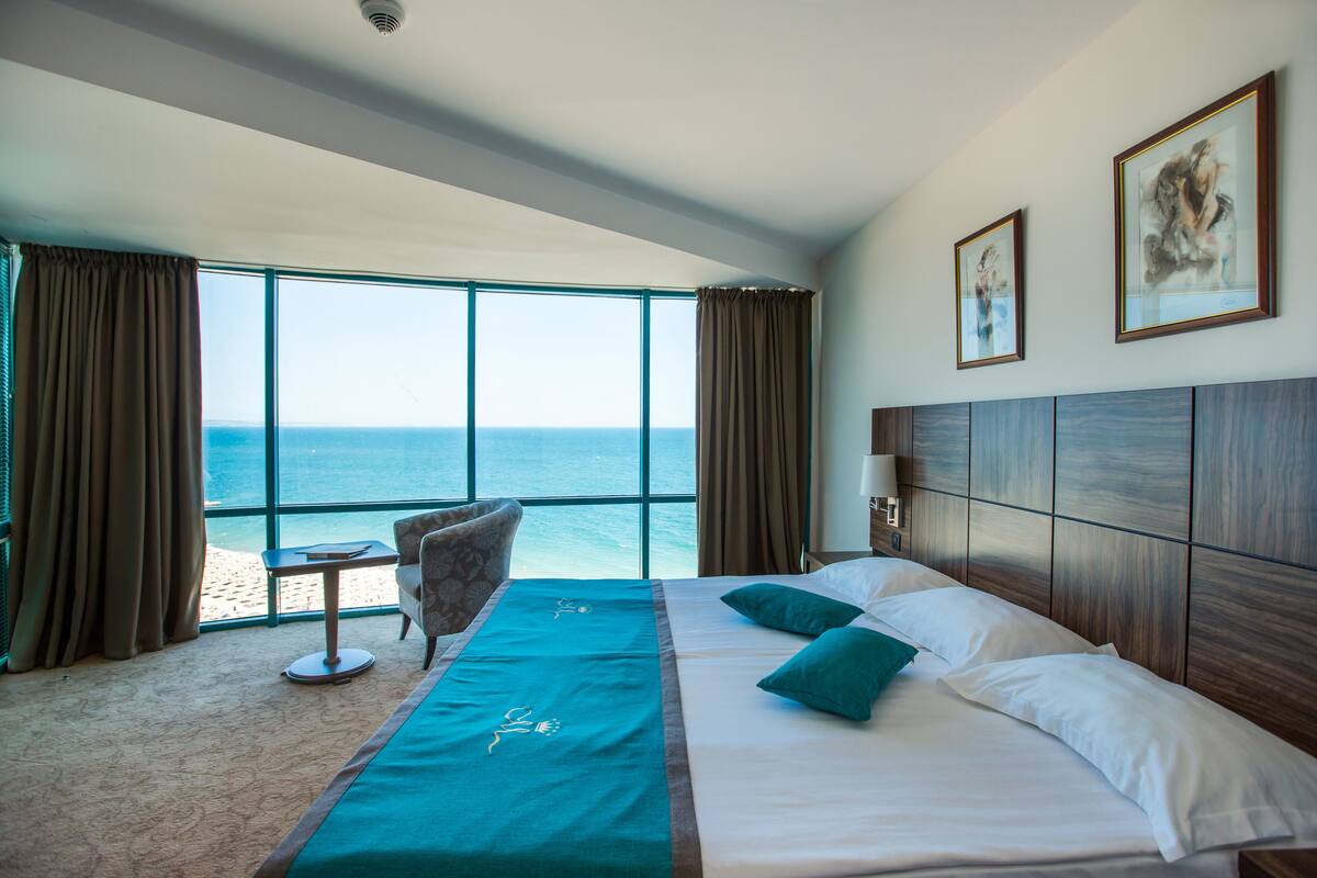 A hotel room with a large window, a bed, a chair, and a small table.