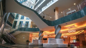 A multi-level atrium with a glass ceiling, a spiral staircase, and a reception area with a lobby bar.