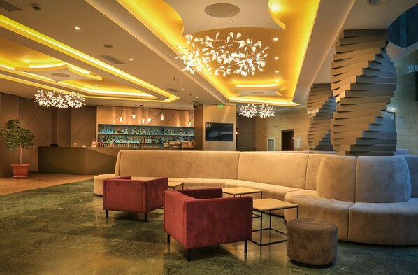 A modern lobby with a large beige sofa, red armchairs, and a bar area with shelves of bottles.