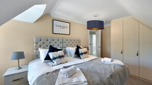 A bedroom with a tufted headboard, a bed with white and black patterned pillows, a bedside table with a lamp, and a framed sign on the wall. - Deanway Serviced Apt Chalfont St Giles (Chalfont St Giles)