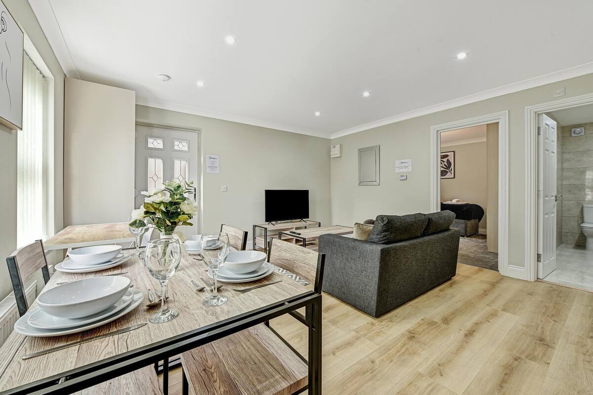 A modern living room with a dining area, a grey sofa, and a flat-screen TV.