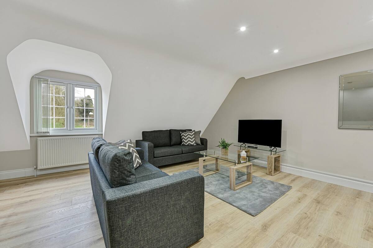A modern living room with a grey sofa, a glass coffee table, and a flat-screen TV.