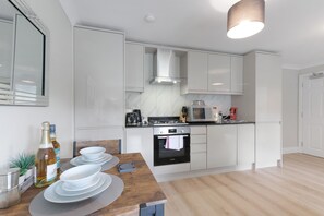 Une cuisine moderne avec des meubles blancs, un four Bosch et un coin repas avec une table en bois, mise pour quatre personnes.