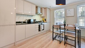 A modern kitchen with light-colored cabinets, a wooden dining table with chairs, and a pendant light. - Deanway Serviced Apt Chalfont St Giles (Chalfont St Giles)