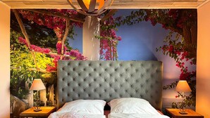 Ein Schlafzimmer mit einem gesteppten Kopfteil, zwei Nachttischen mit Lampen und einem floralen Wandbild.