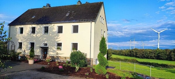 Ein zweistöckiges Haus mit geneigtem Dach, zahlreichen Fenstern und einem gepflegten Garten mit verschiedenen Pflanzen und Blumen.