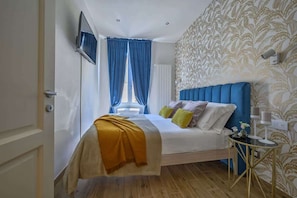 A bedroom with a bed, curtains, a TV, a wall-mounted lamp, and a patterned wallpaper.