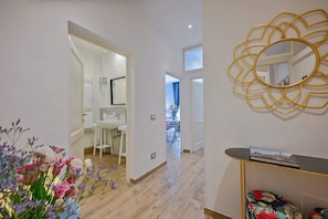 A modern interior with a hallway leading to a dining area, a white bathroom, and a decorative gold mirror.