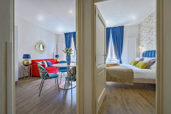 A hotel room with a bed, a red sofa, a dining table, and a chair.