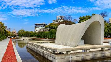 A modern architectural structure with a curved design, surrounded by a water feature and a pathway with red foliage.
