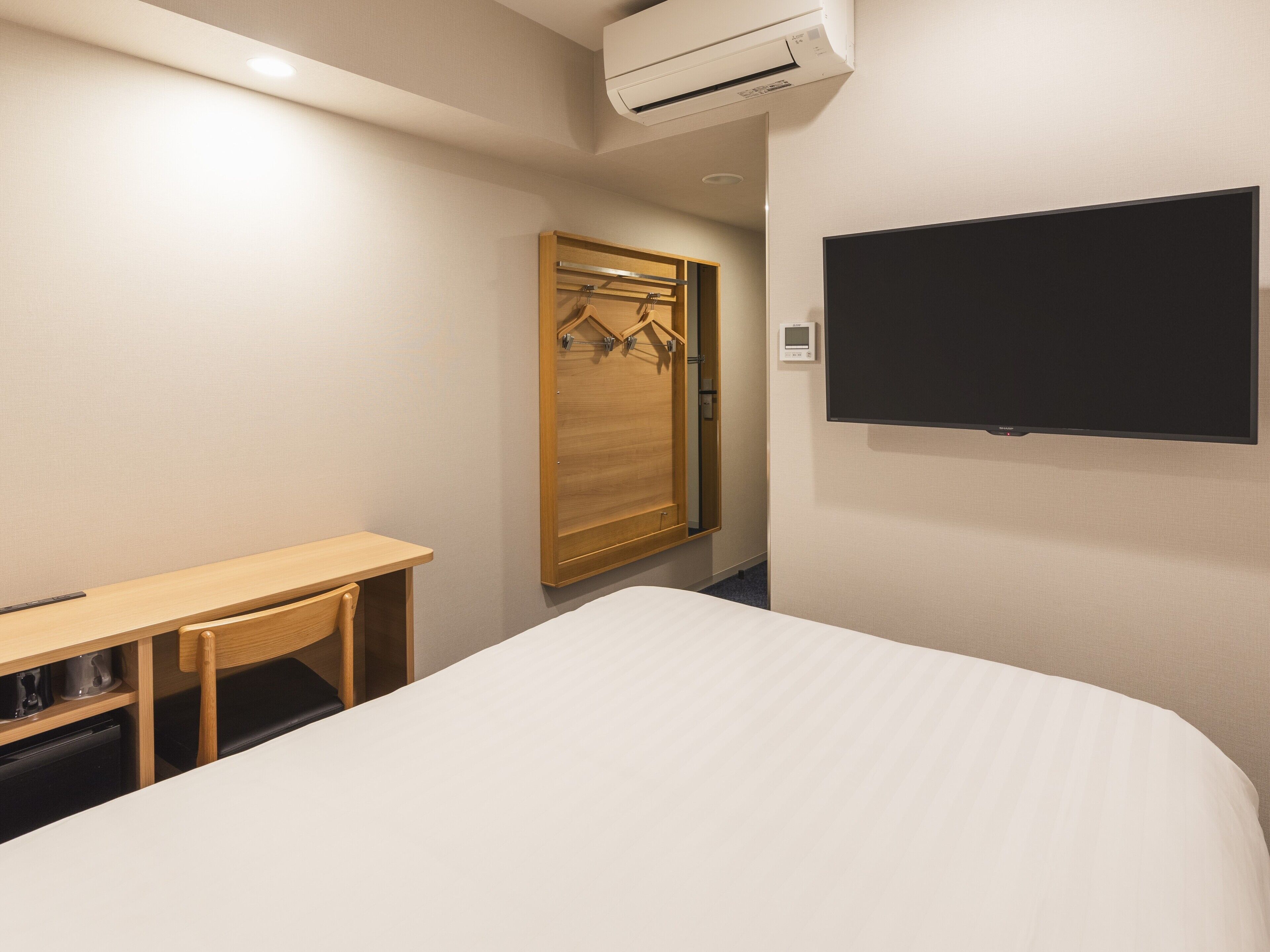 A hotel room with a bed, a desk, a wardrobe, and a mounted TV.