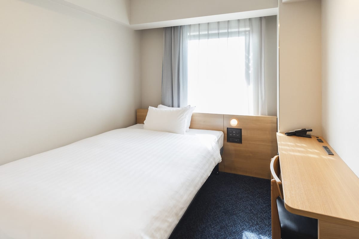 A hotel room with a single bed, a desk, and a window with curtains.