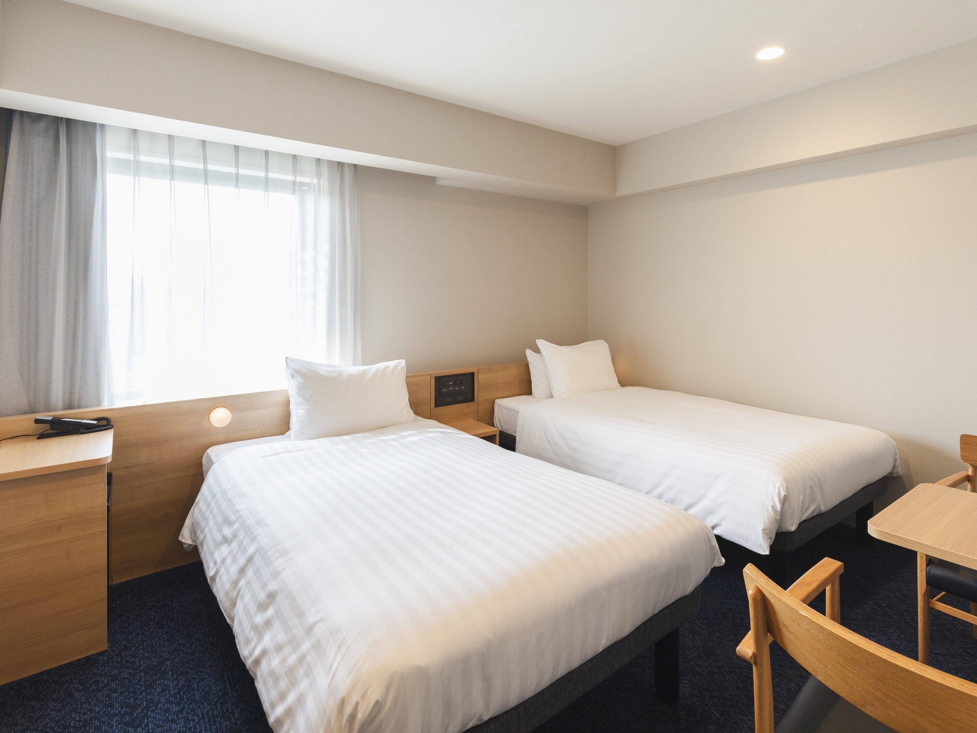 A hotel room with two beds, a desk, and a chair.