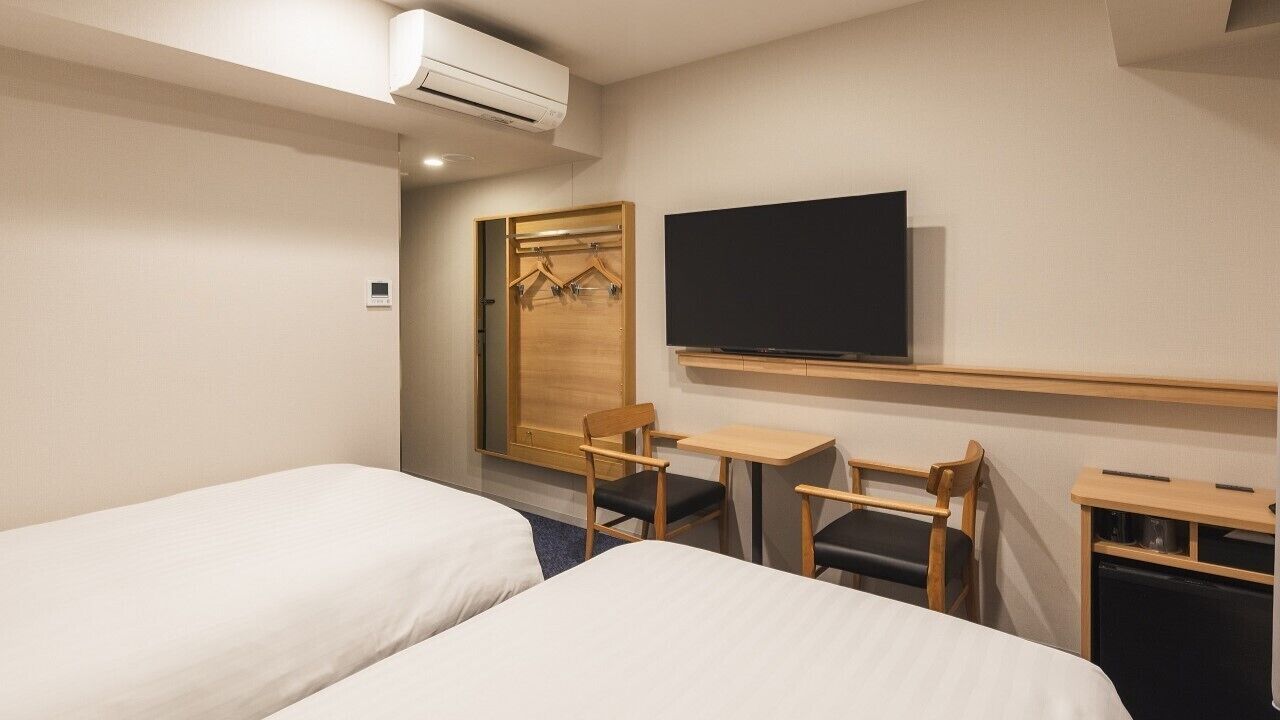 A hotel room with two beds, a TV, a desk, and a wardrobe.