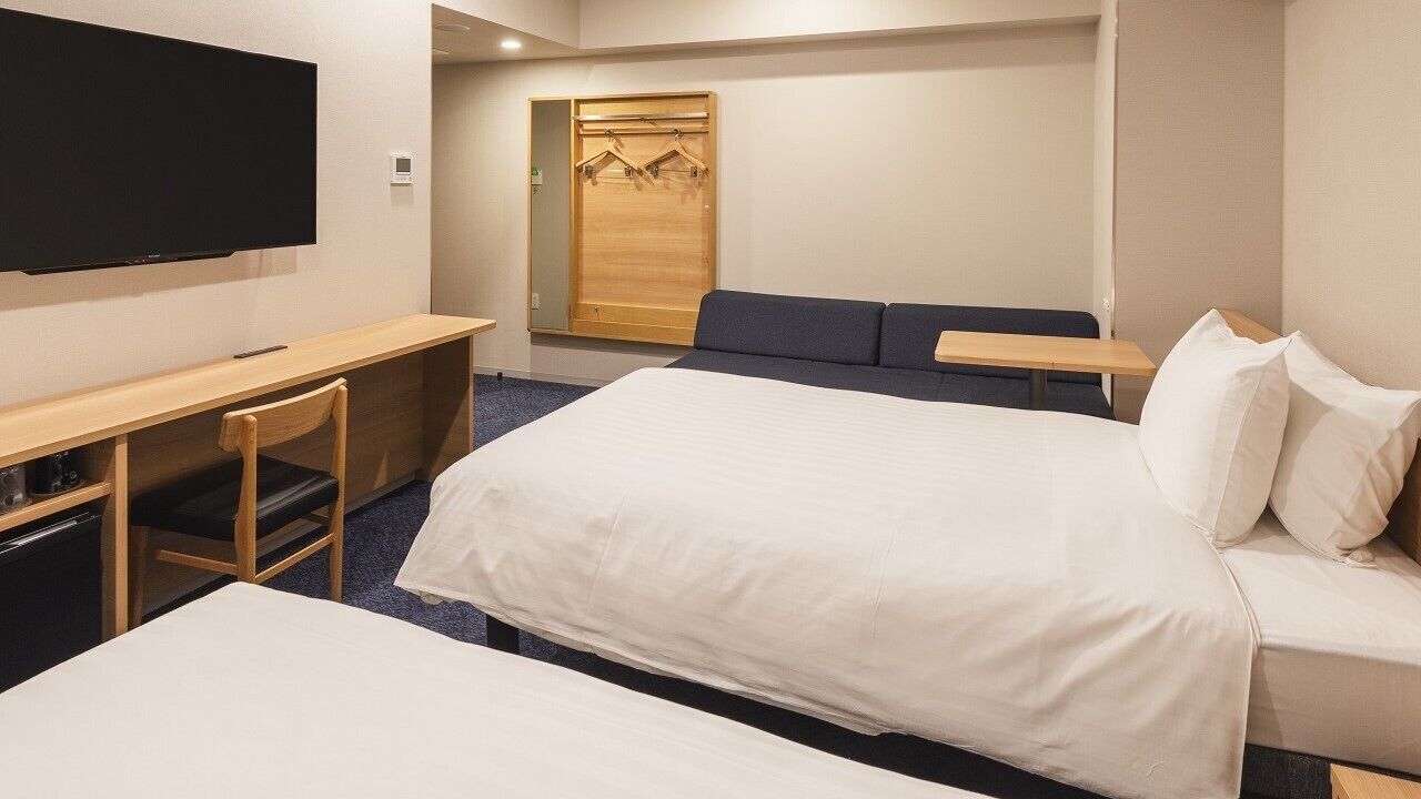 A hotel room with a bed, a desk, a chair, a TV, and a wardrobe.