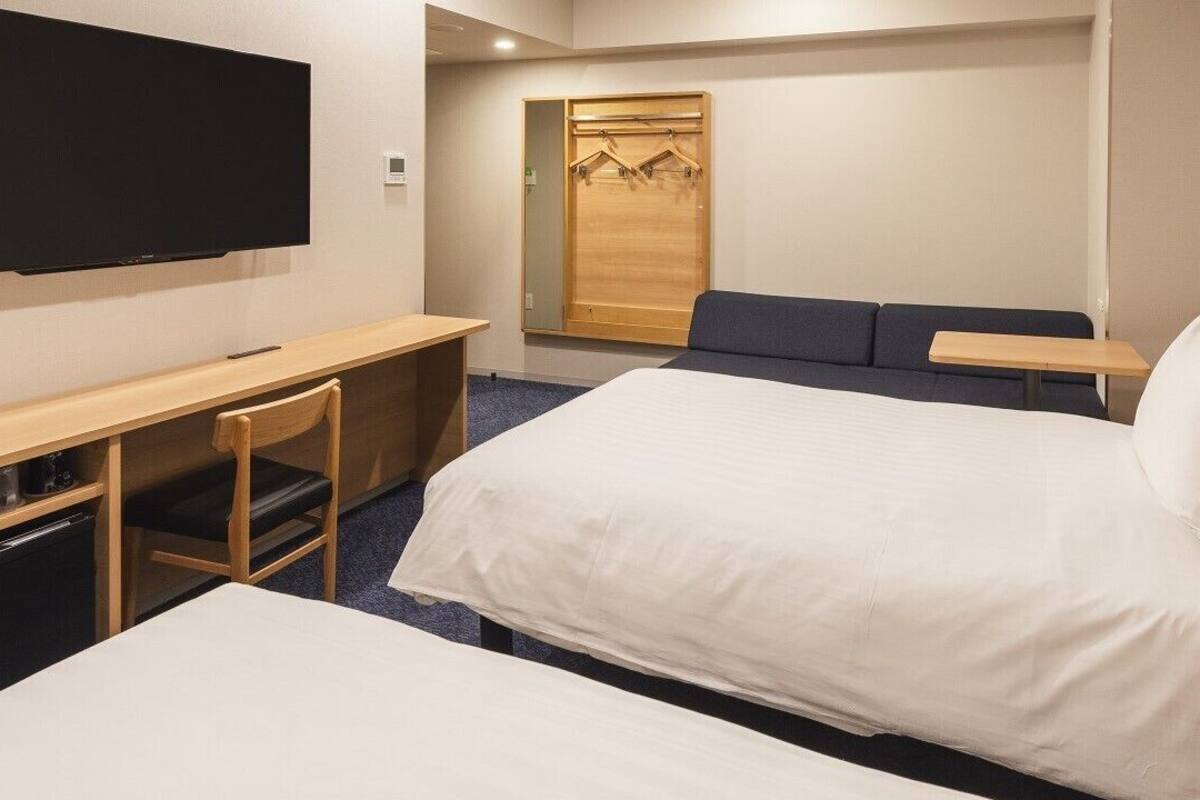 A hotel room with a bed, a desk, a chair, a TV, and a wardrobe.