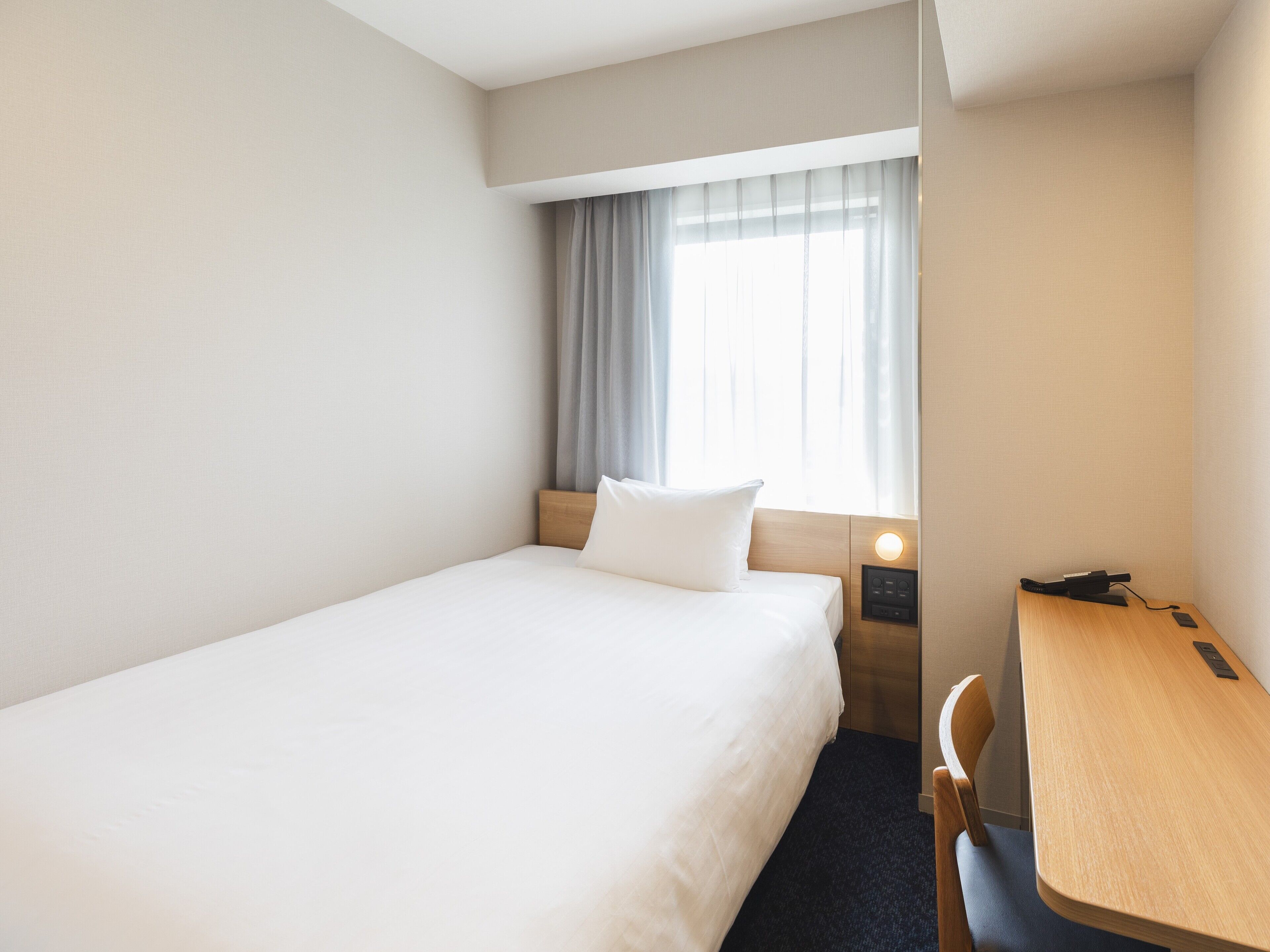 Ein Hotelzimmer mit einem Einzelbett, einem Schreibtisch und einem Stuhl.