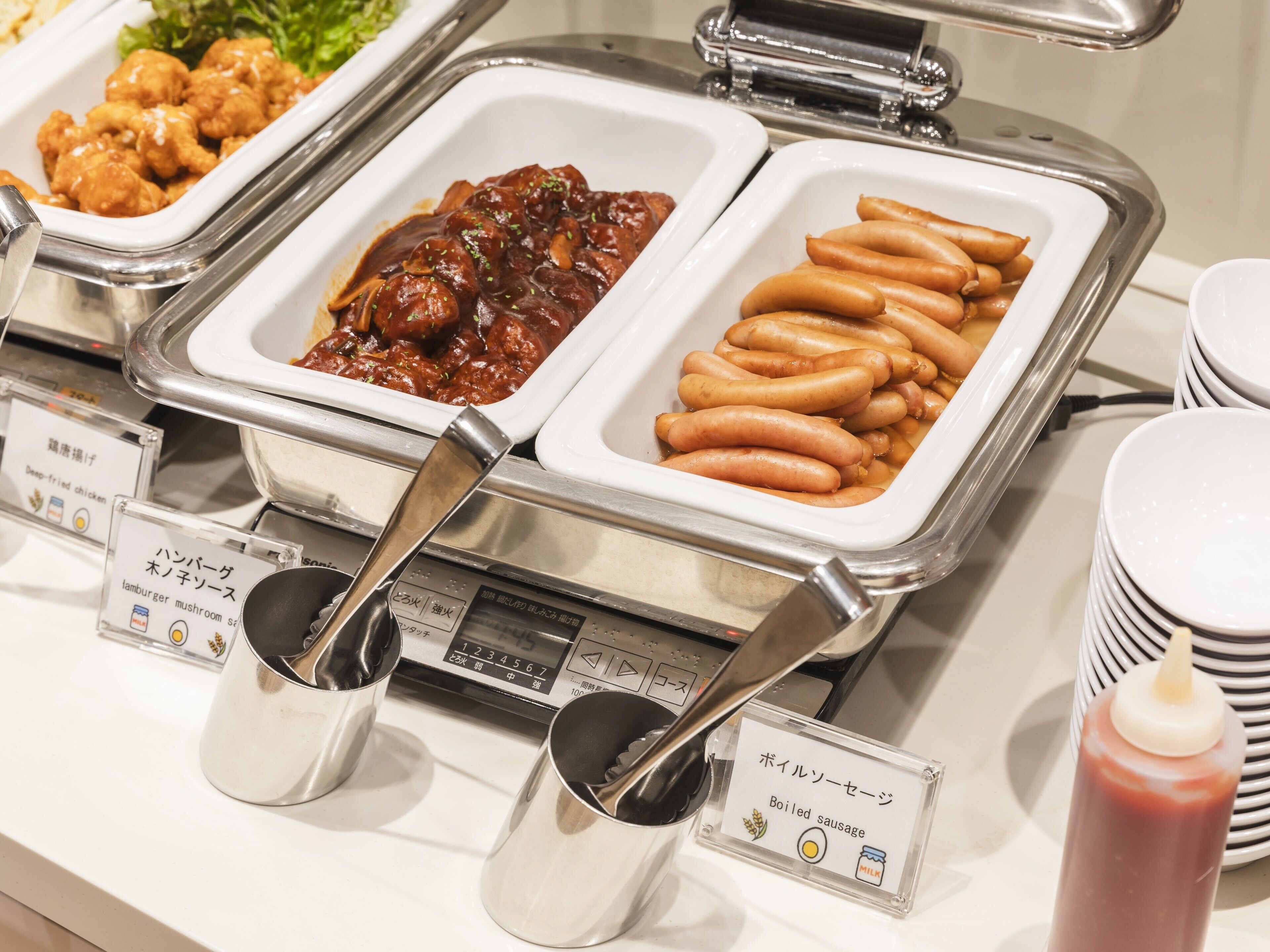 Ein Buffet mit beschrifteten Behältern, darunter frittiertes Hähnchen, Pilzwurst und gekochte Wurst.