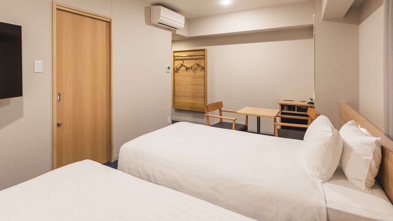 A hotel room with two beds, a desk, a chair, a wardrobe, and a television.