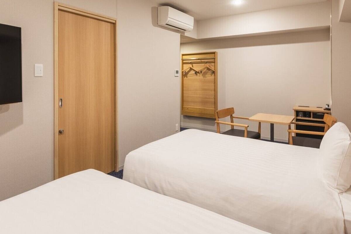 A hotel room with two beds, a desk, a chair, a wardrobe, and a television.