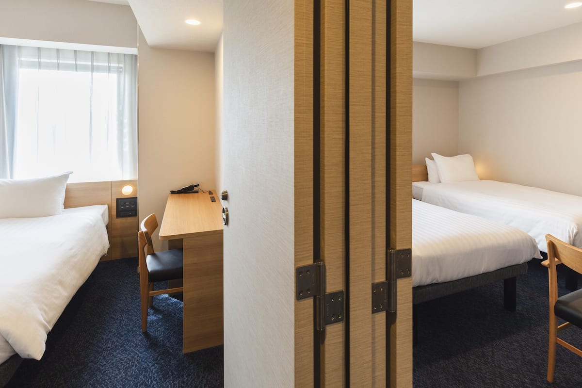 A hotel room with two single beds, a desk with a chair, and a small table with a phone and a lamp.