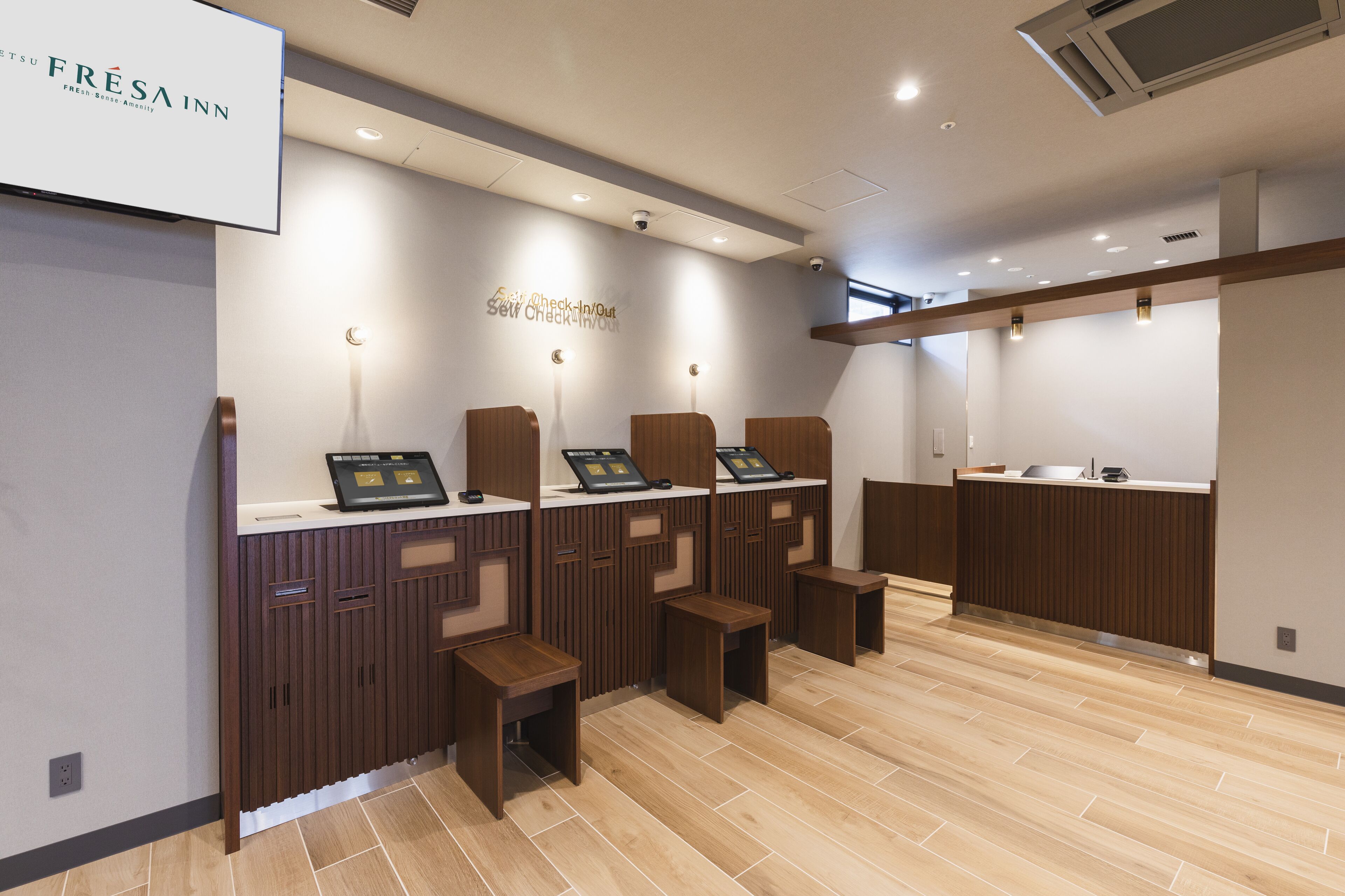 A modern check-in/out area with self-service kiosks, wooden counters, and a clean, tiled floor.