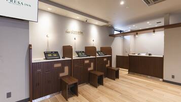A modern check-in/out area with self-service kiosks, wooden counters, and a clean, tiled floor.