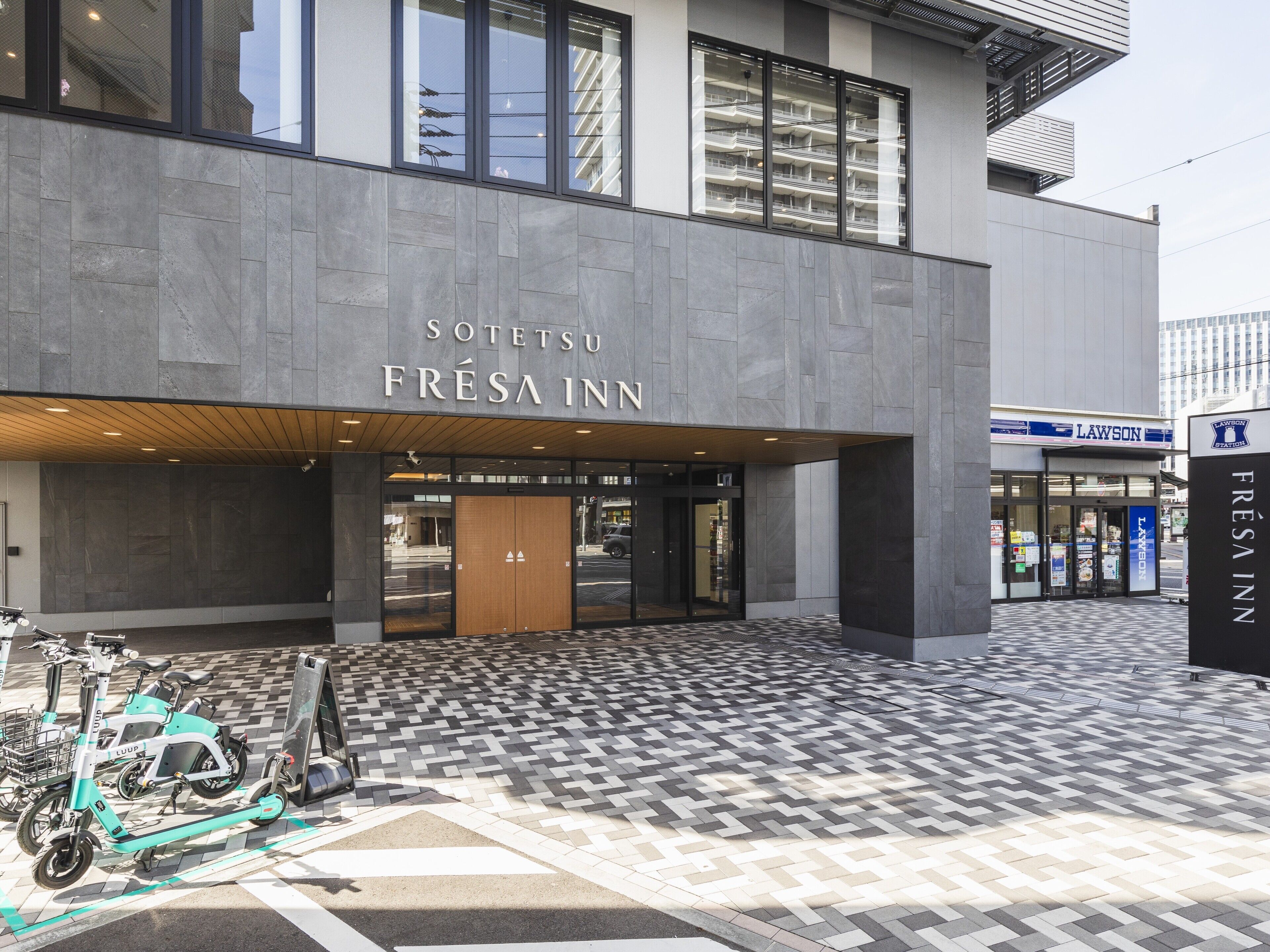El exterior del hotel SOTETSU FRÉSA INN, con un diseño moderno, amplias ventanas y un pavimento a cuadros en la entrada.