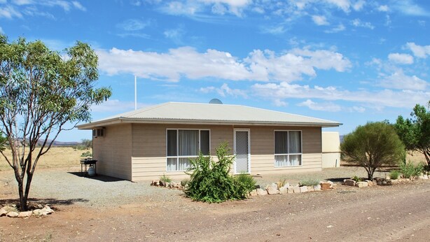 A single-story house with a flat roof, a small porch, and a gravel driveway.