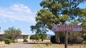 A sign for Homestead Cottage with a dirt road leading to it, surrounded by trees and a clear sky.