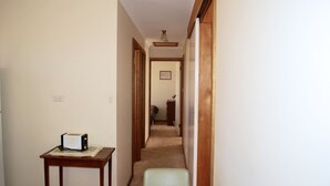 A narrow hallway with a wooden table and a green chair on the left, leading to a bedroom with a bed and dresser.