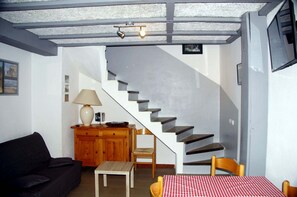 A living room with a sofa, a table with a checkered tablecloth, a lamp, a wooden cabinet, and a staircase.