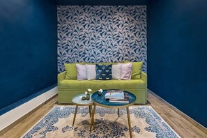 Une pièce avec un canapé vert, deux tables rondes, un tapis à motifs et un mur bleu à motifs.