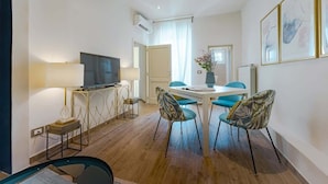 A modern hotel room with a flat-screen TV, a dining area with a table and chairs, and a large window with curtains. - Macci A) Modern Elegant Apartment S. Ambrogio (Firenze)