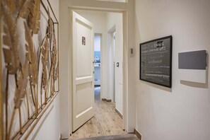 A hallway with a door leading to a bathroom, a framed sign on the wall, and a decorative wall piece.