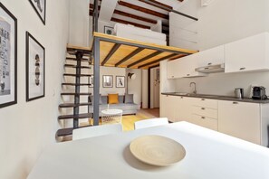 A compact kitchen with a dining area, a loft bedroom with a wooden ladder, and a staircase.