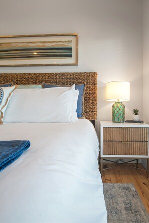 A neatly made bed with white bedding, a woven headboard, a bedside lamp, and a small plant on the nightstand. - Views! Heated Private Pool* | Golf Cart  3rd nt FREE thru Nov! (Port Aransas)