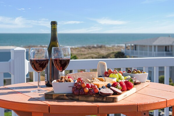 A table with a cheese board, grapes, strawberries, and a bottle of wine, set against a coastal backdrop. - Views! Heated Private Pool* | Golf Cart  3rd nt FREE thru Nov! (Port Aransas)