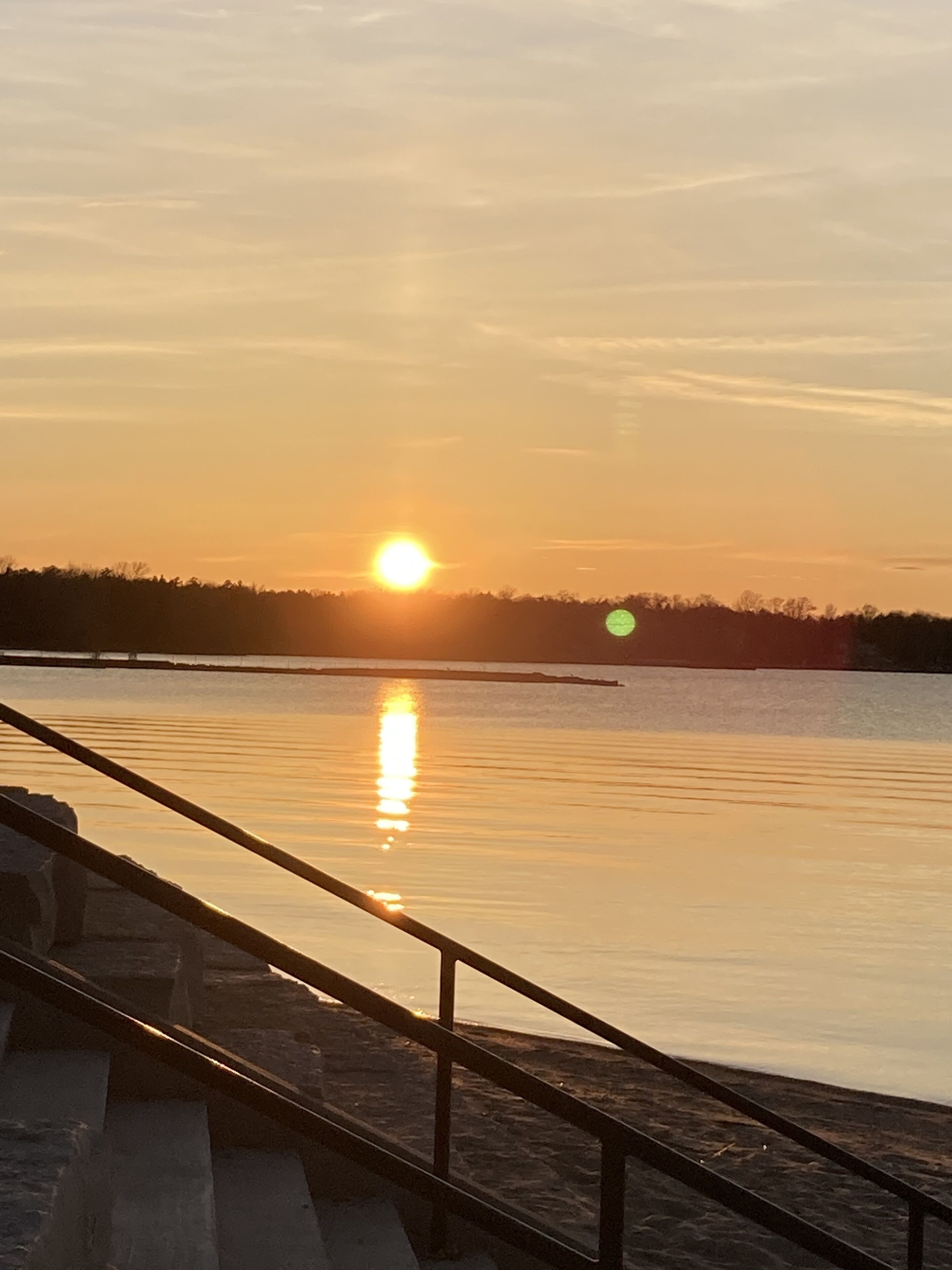 Un coucher de soleil sur une étendue d'eau calme, avec un pont au premier plan.